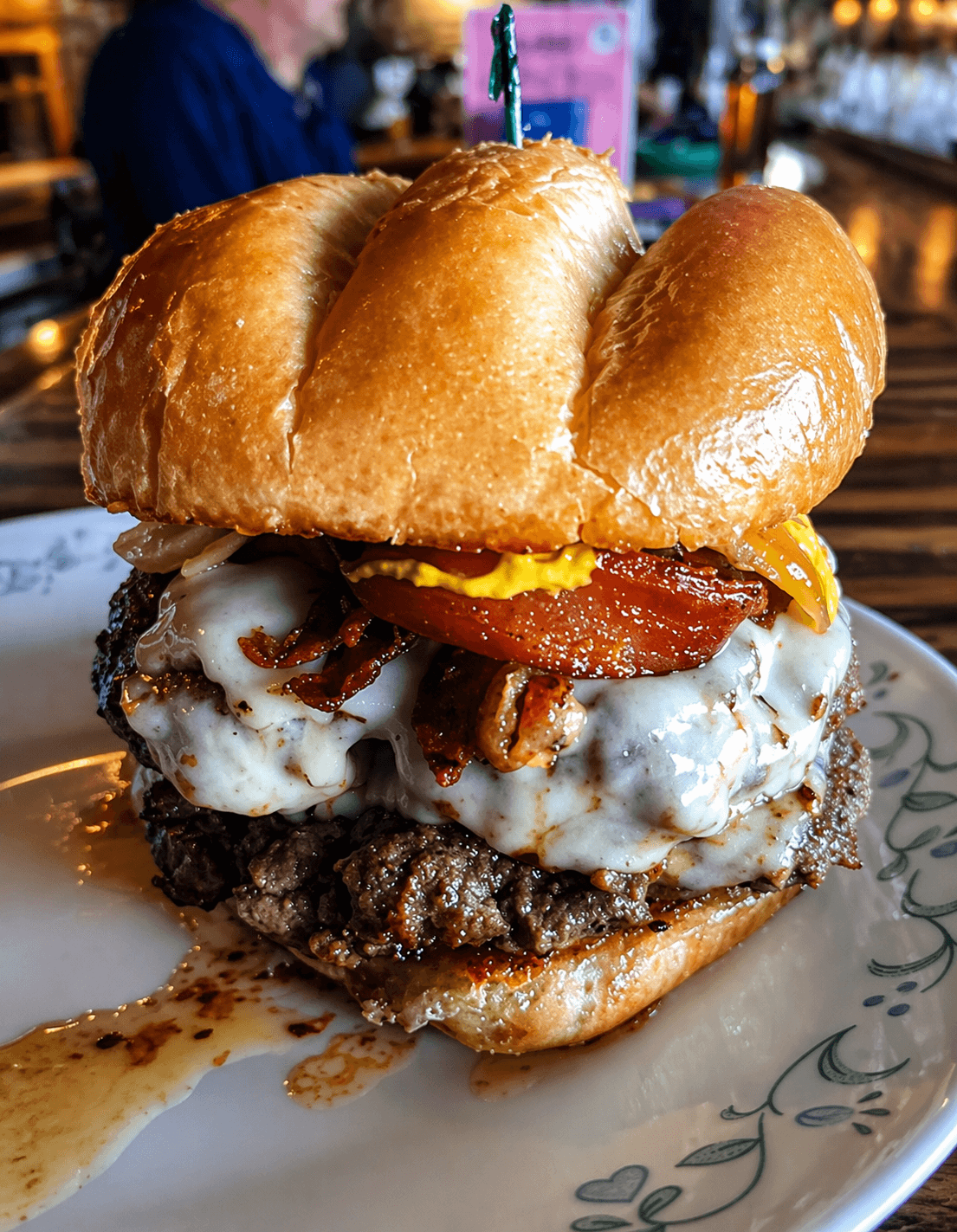 Close-up of a BoRocks burger with cheese, bacon, tomato, pickle, and glossy bun